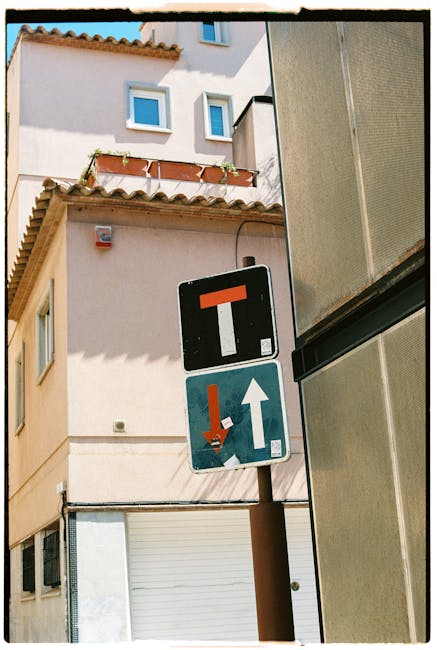 A height restriction traffic sign on a brown metal pole positioned on a narrow street in Dalston E8, showing a black square with a red horizontal bar indicating no through passage for vehicles over a